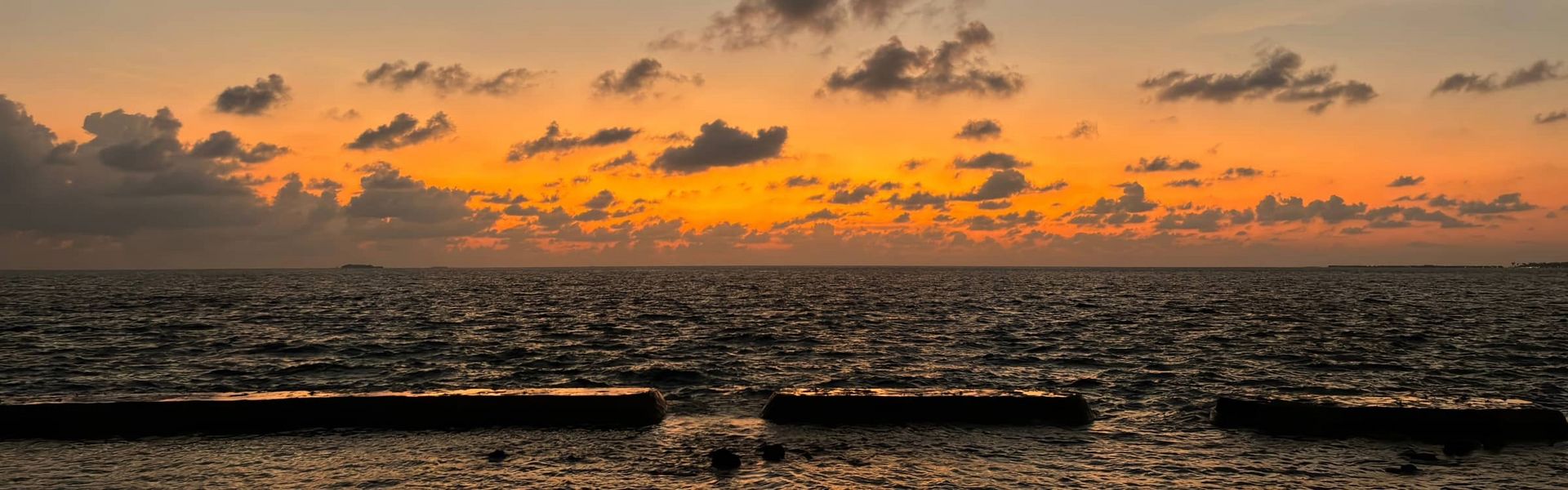 Ein ruhiges Meer bei Sonnenuntergang, das orangefarbene Licht der untergehenden Sonne spiegelt sich an den Wolken und am Horizont.