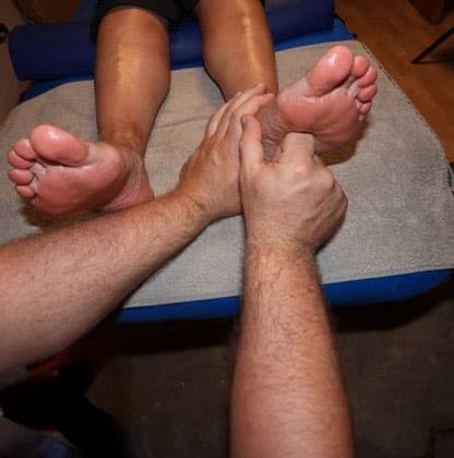 Nahaufnahme einer Fußmassage mit zwei Händen auf einem blauen Handtuch.
