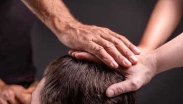 Zwei Hände legen sich sanft auf den Kopf einer Person, symbolisieren Heilung und spirituelle Unterstützung.