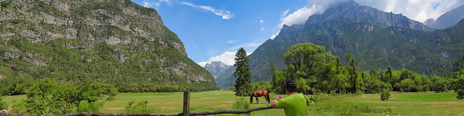 Über mich Wiese mit grasendem Pferd und Bergen im Hintergrund, fotografiert von einer Person an einem sonnigen Tag.